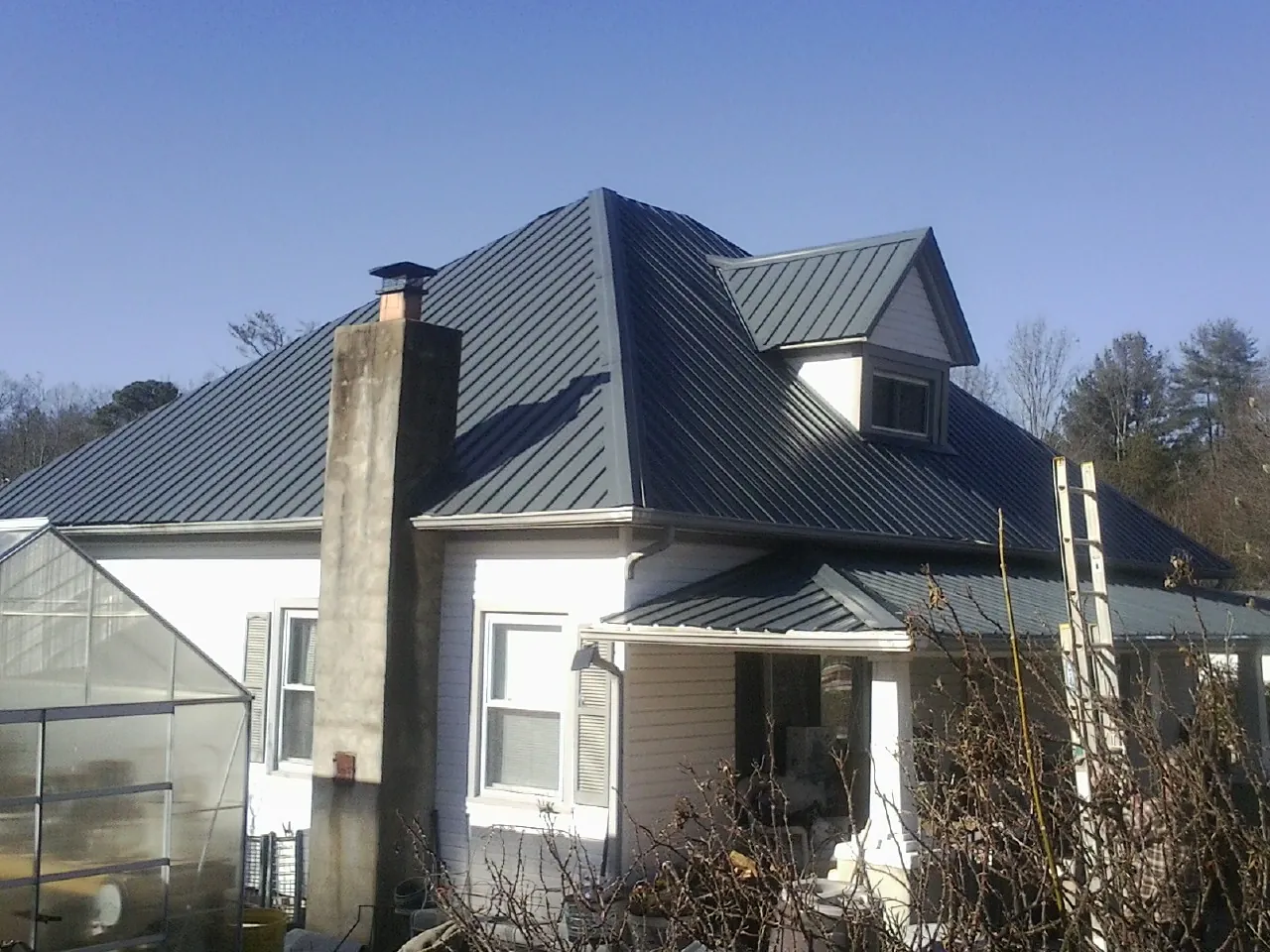 Dark blue standing seam metal roof on a white farmhouse with dormer — Slate & Tile Roof Repair by Roofing Brothers in Kirkwood
