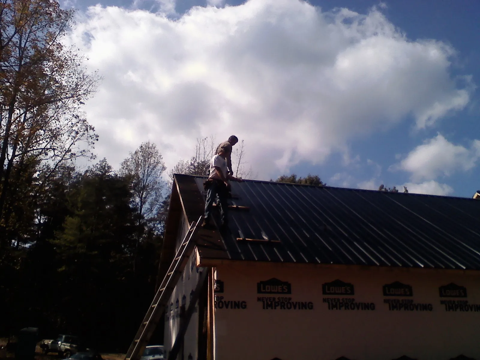 Roofer fastening dark metal panels high against a cloudy sky, from a Roof Inspection job in Kirkwood