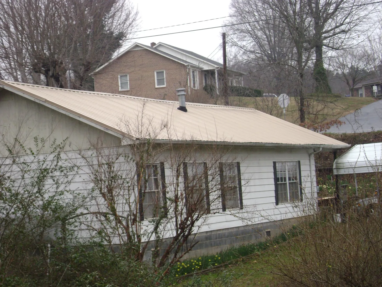 Tan metal roof on a white sided house set into a hillside — Commercial Roofing by Roofing Brothers in Kirkwood